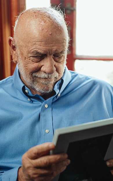 older man in a blue shirt looking at a photo of loved ones and smiling