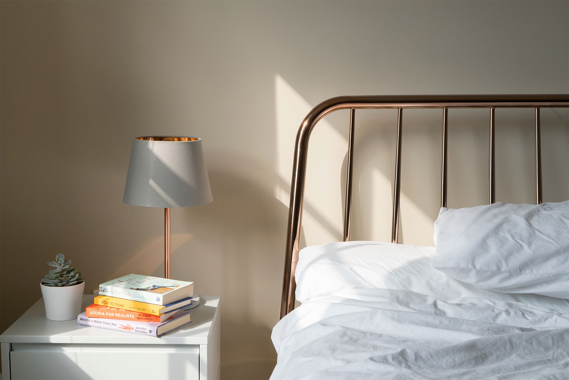 a made up bed with a golden frame and a bedside table with a lamp and stack of books