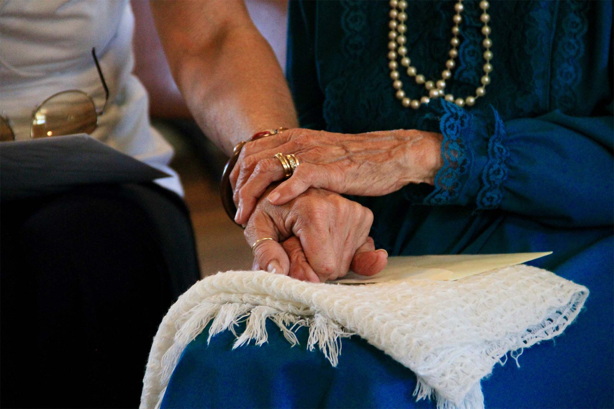 resident and carer holding hands in support while sat down togetherq