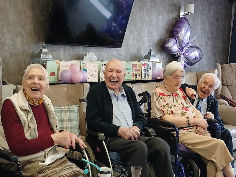 4 residents sat in wheelchairs in the lounge smiling and laughing together