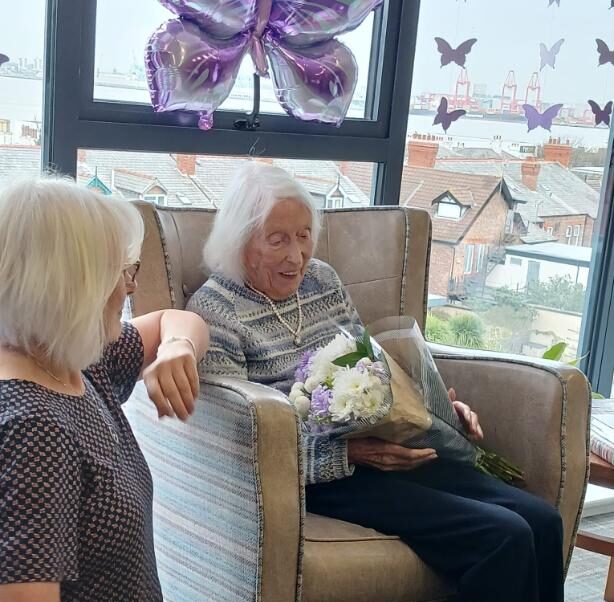 an older lady sat down in a chair with some flowers