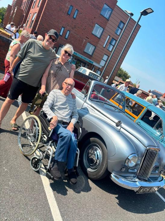 older man in wheelchair with others by car