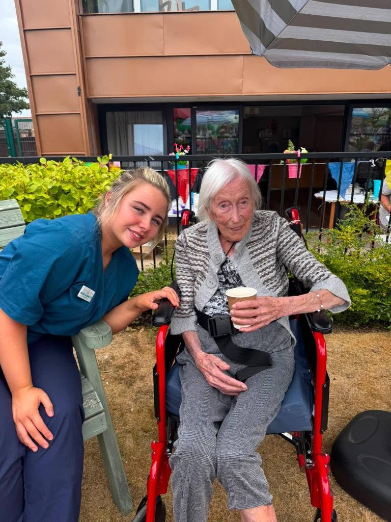 resident holding coffee sat next to carer